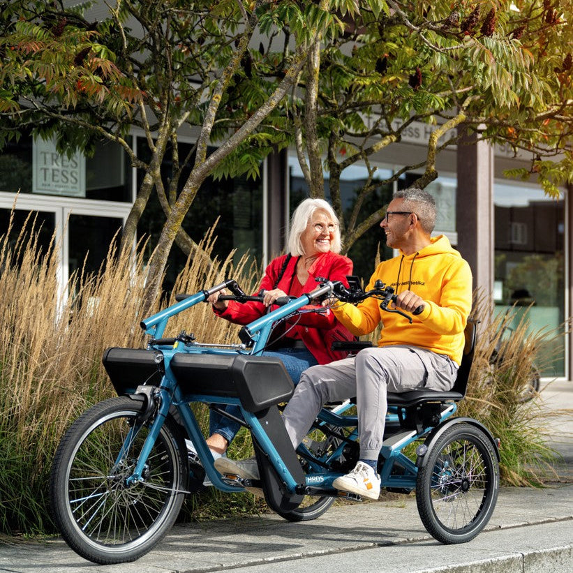 Lady and man smiling at eachother while riding the Huka Orthros Tandem Tricycle