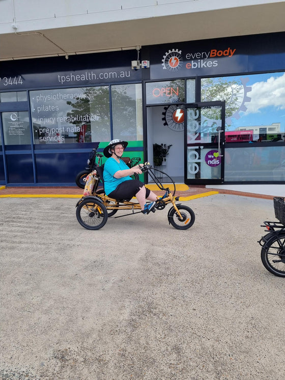 Happy customer outside everyBody ebikes riding a gold Trident semi-recumbent electric tricycle
