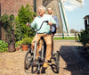 Smiling elderly man riding Huka Co-Pilot 3 Tandem Tricycle with support person in the back 