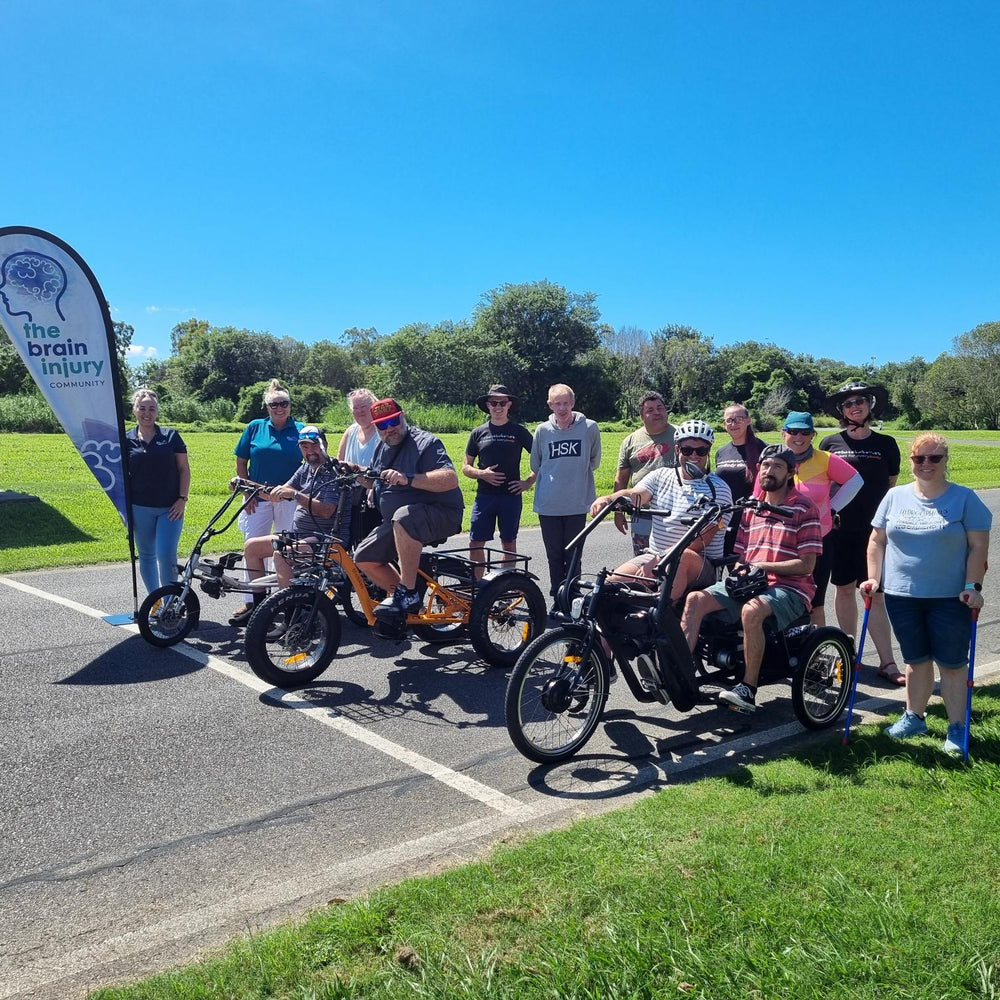 A group from The Brain Injury Community Group in Brisbane at a bike riding come and try event. Attendees are riding a range of electric tricycles including independent upright trikes, sit-down semi-recumbent trikes and a side-by-side tricycle