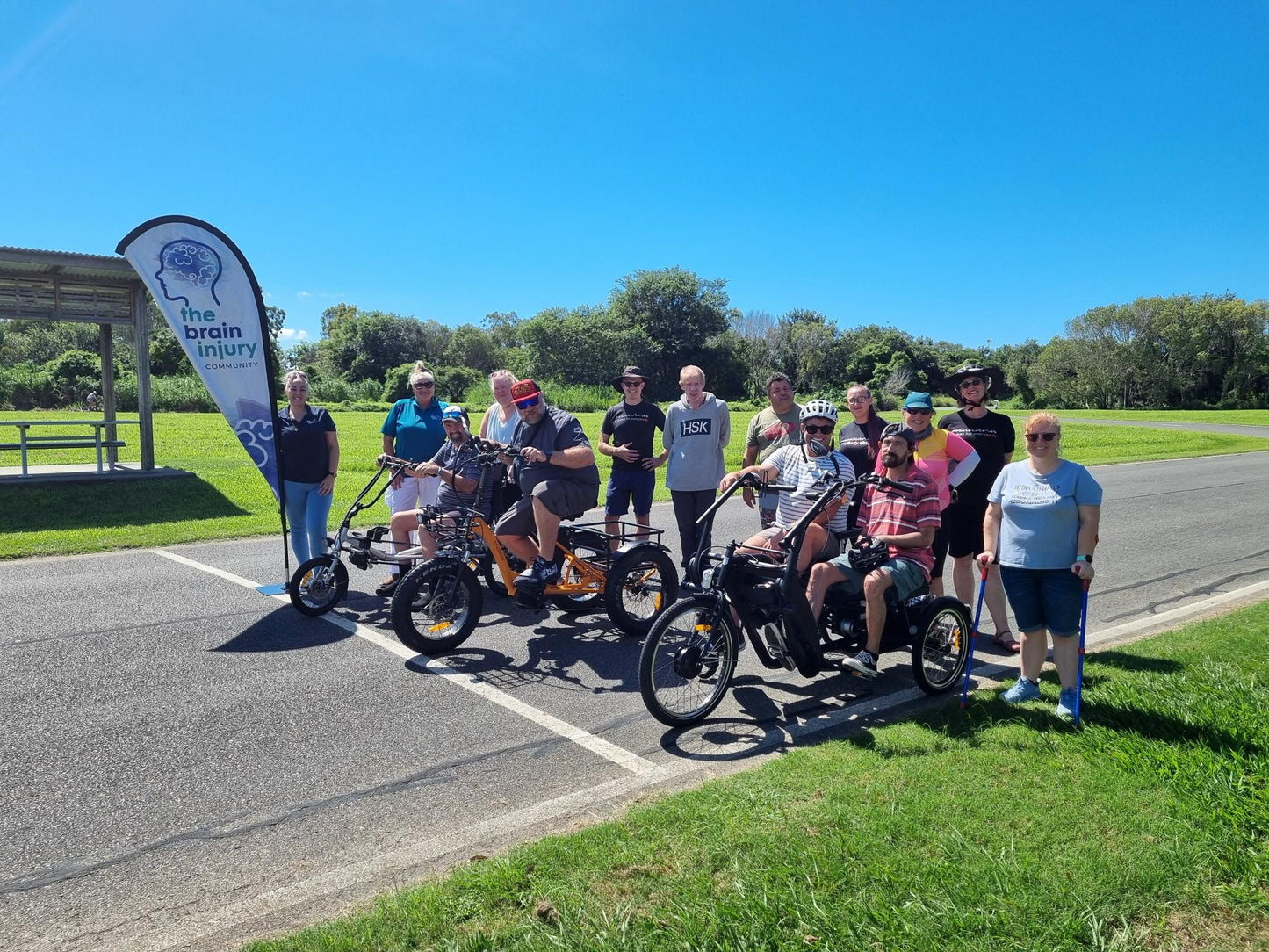 A group from The Brain Injury Community Group in Brisbane at a bike riding come and try event. Attendees are riding a range of electric tricycles including independent upright trikes, sit-down semi-recumbent trikes and a side-by-side tricycle