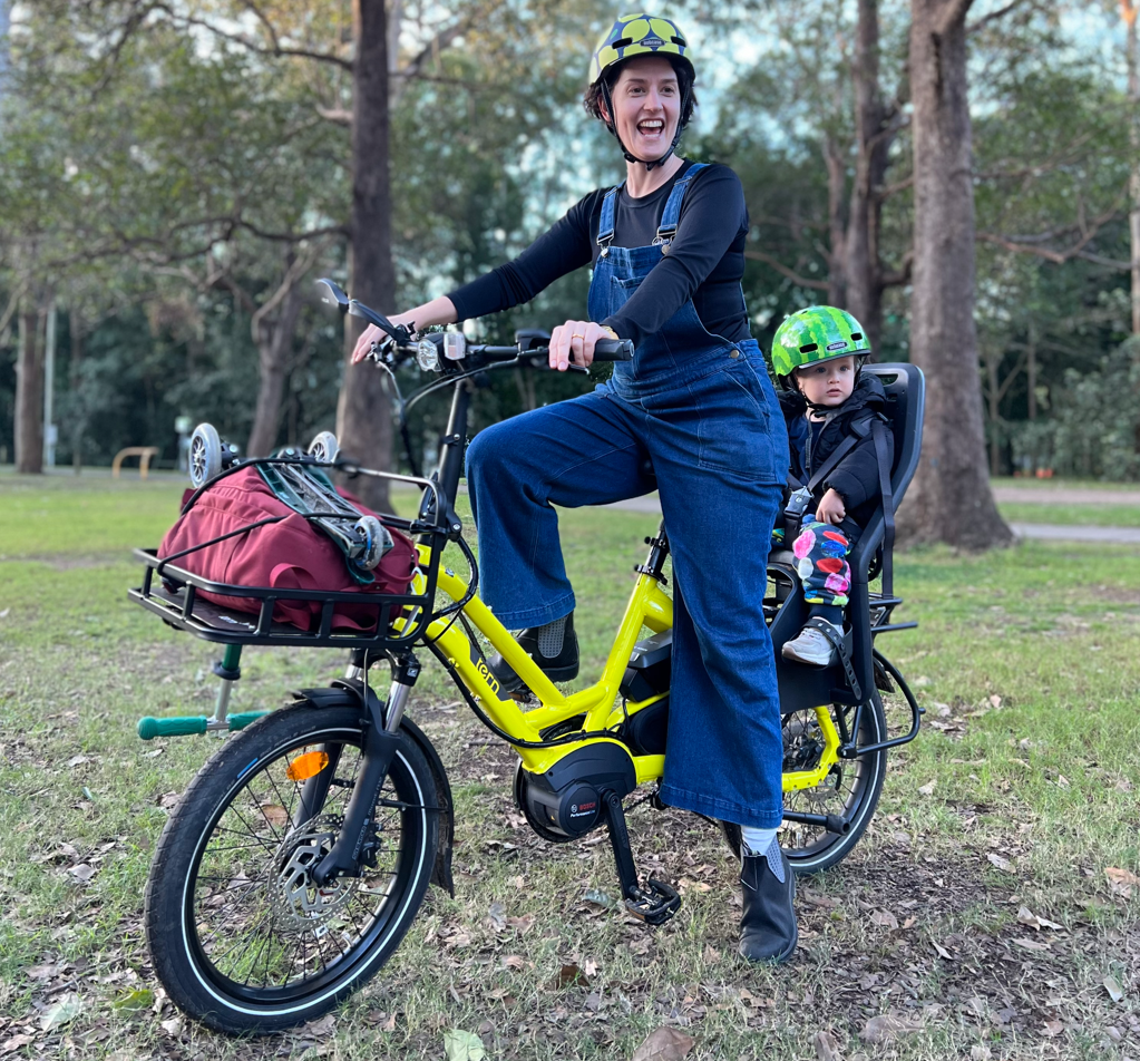 Lady with child on rear of short-tailed cargo back and red bag on the front enjoying the outdoors