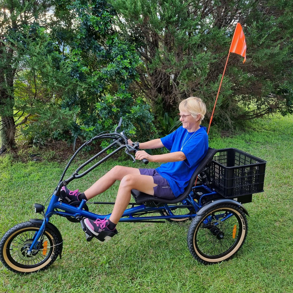 Women sitting on blue sit-down trike, semi-recumbent electric tricycle Trident with black crate at rear and orange flag