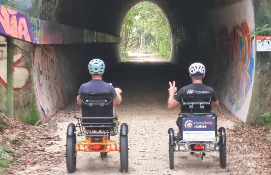 Two people riding on sit-down tricycles through a tunnel on a rail trail NRRT