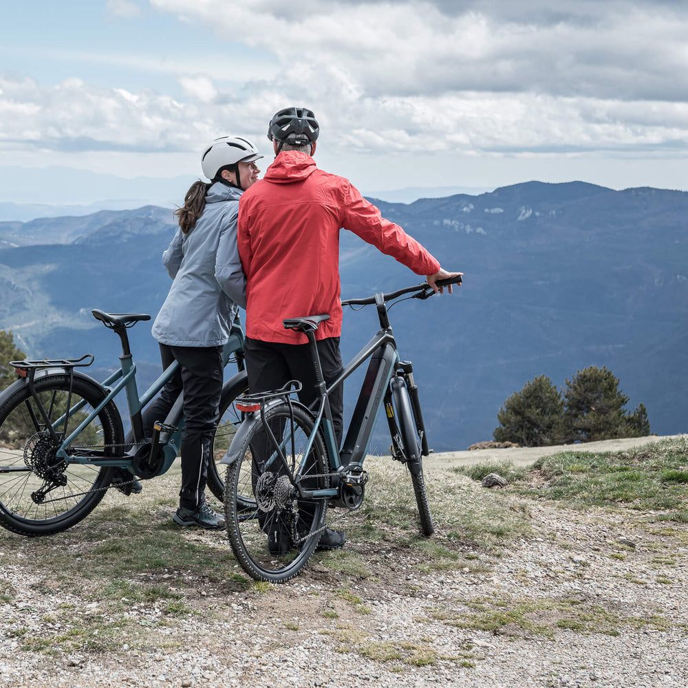 Two people riding mid-drive Kalkhoff electric bikes, standing overlooking mountains in the distance