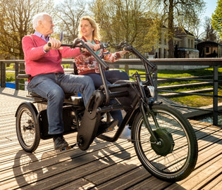  Two people sitting on a side-by-side Huka Orthros trike smiling and enjoying each others company