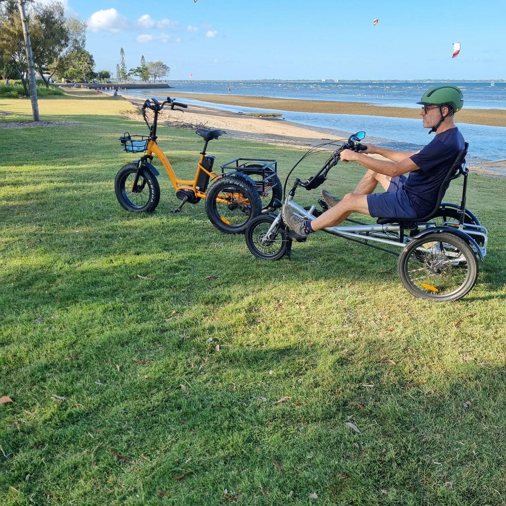 
                      
                        Man siting on silver coloured Trident semi-recumbent electric tricycle next to a orange coloured tricycle
                      
                    