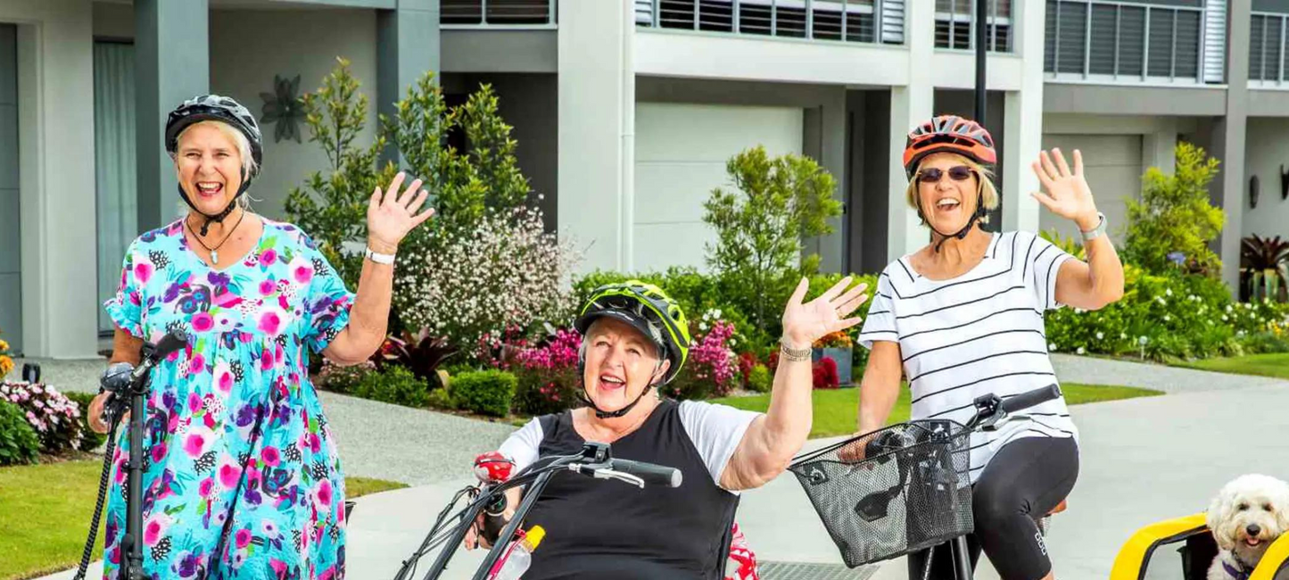 Three elderly waving while on their electric bikes & trikes