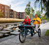 Smiling lady and man riding blue Huka Orthros Tandem Tricycle