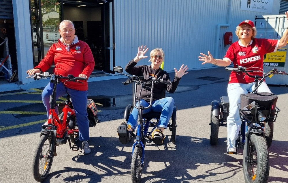 Three people on electric trikes in front of a building