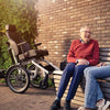 Smiling man sitting on a bence next to his Huka Diaz Electric Wheelchair Tandem Trike