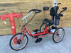 Red special needs electric tricycle next to wooden wall